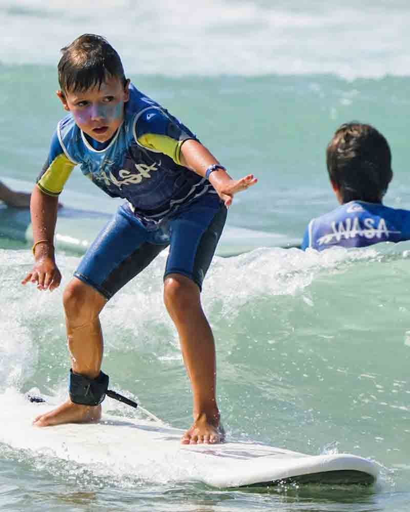 enfant sur une planche en mousse dans la vague pendant un cours de surf enfant