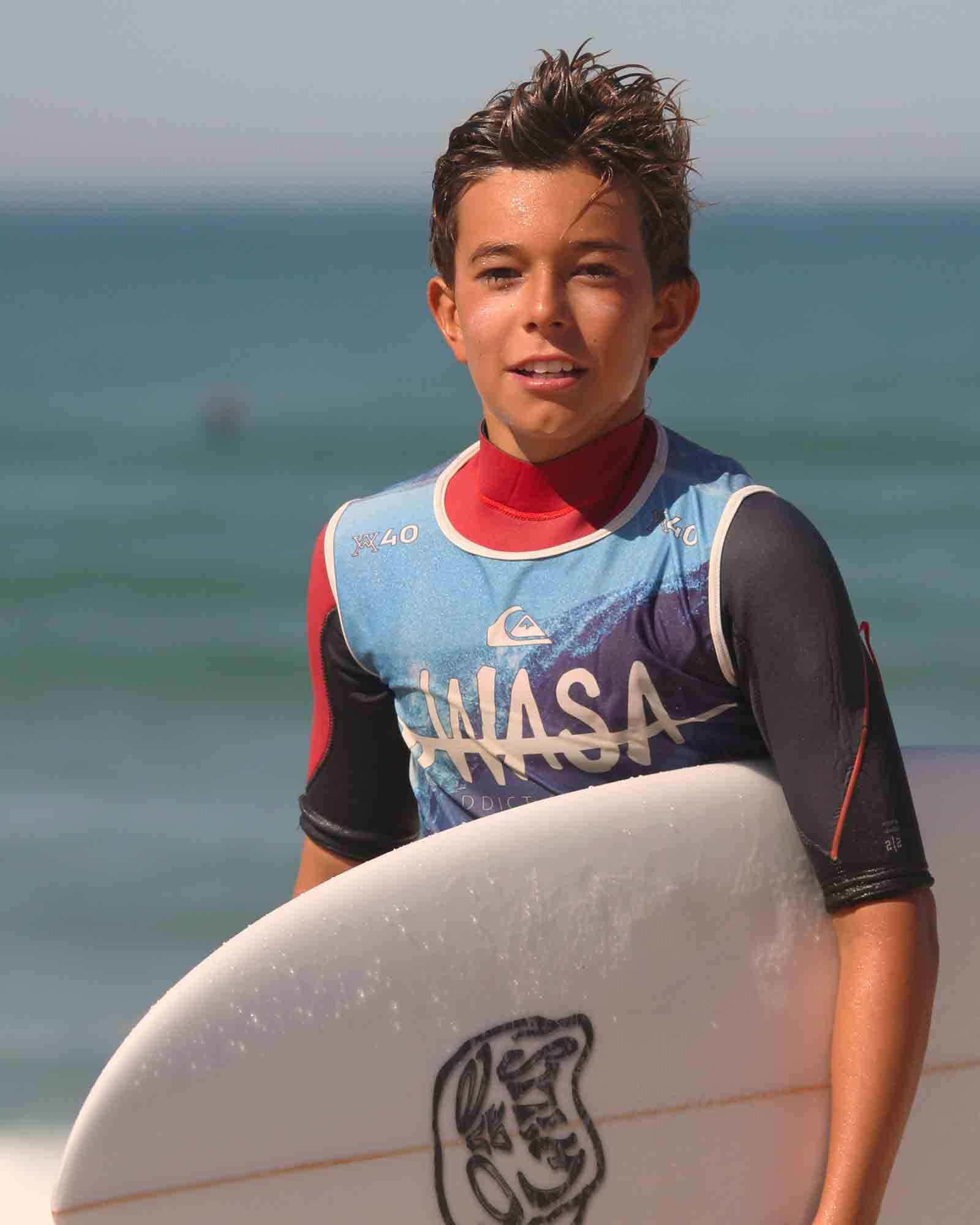 ado tenant sa planche et marchant sur le sable avec lycra bleu de l'école de surf wasa